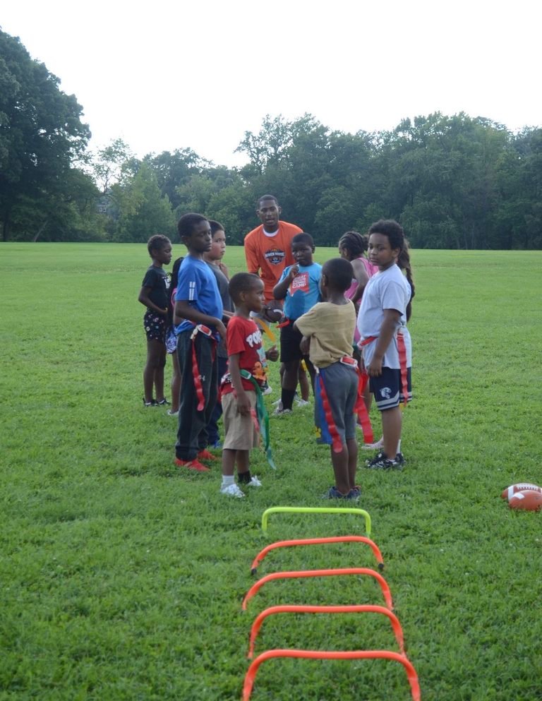 Young athletes gather around a coach at flag football practice.